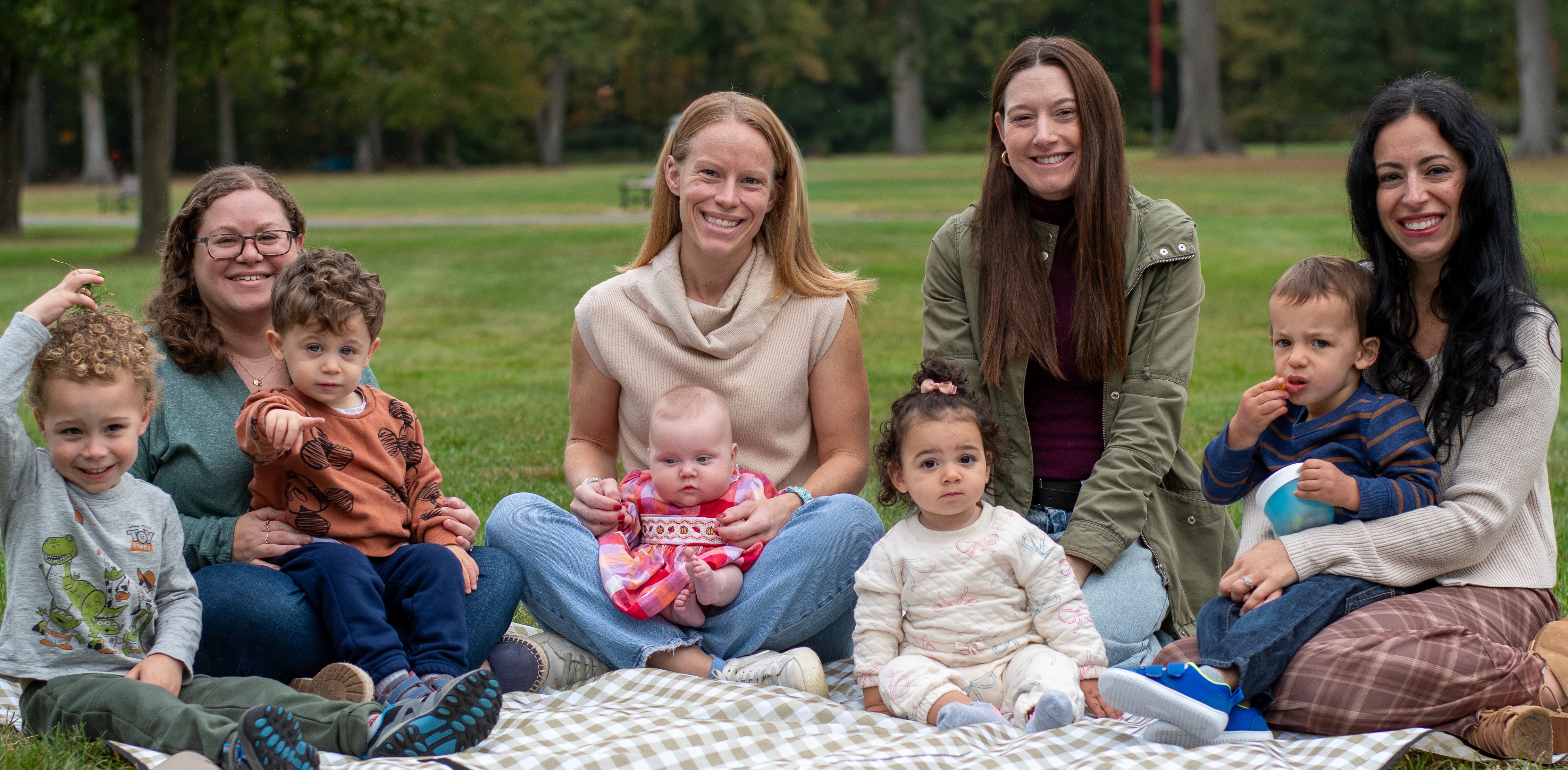 A group of Mothers' Center members and their young children enjoying time together in a park.